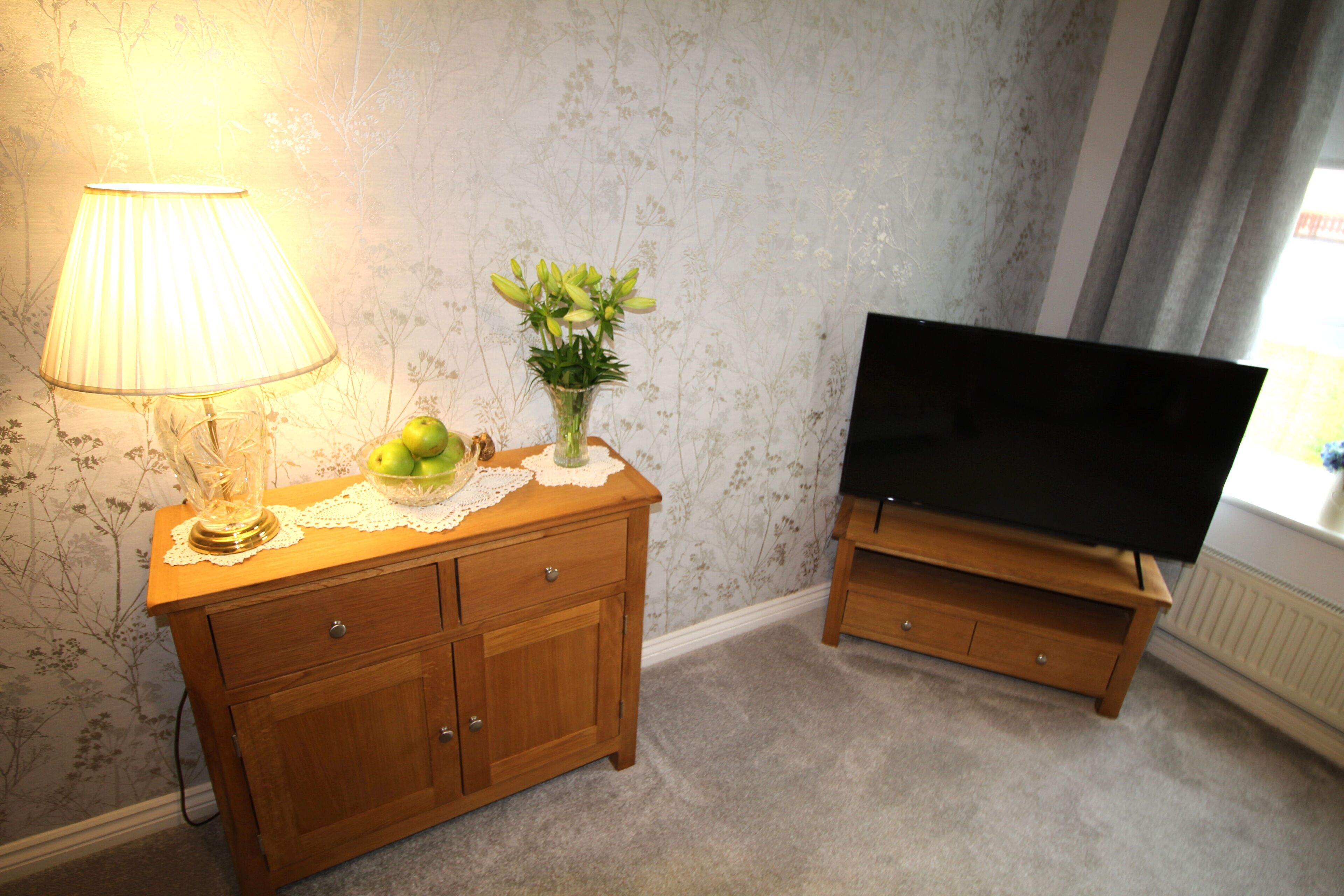 Ein Holzkabinent mit einer Lampe, einer Blumenvase und einem Fernseher auf einem Schrank.