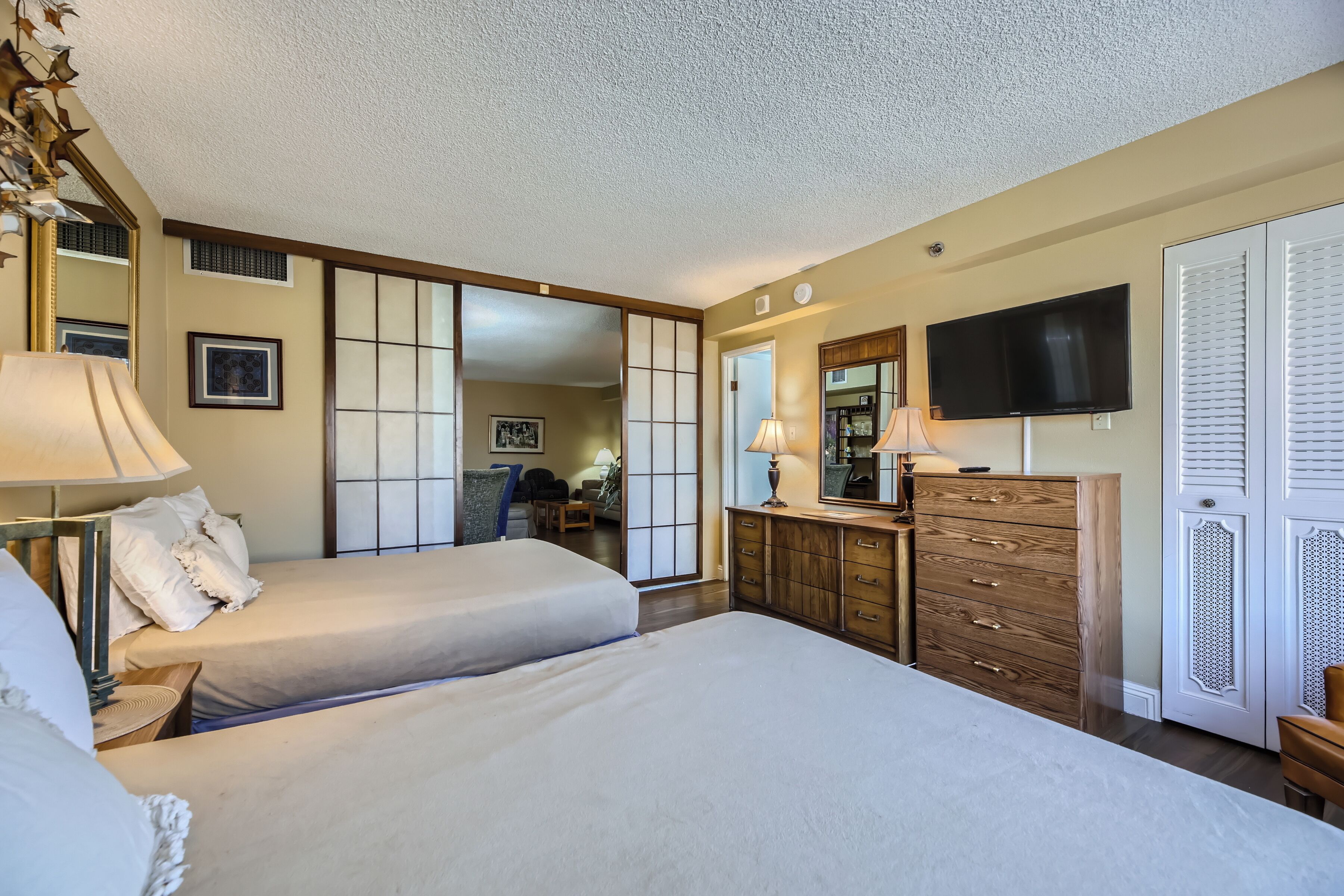 A hotel room with two beds, a TV, a dresser, and a sliding shoji screen door.