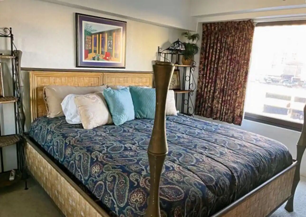 A bed with a patterned bedspread, a headboard, and a tall, slender bedside table.