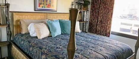 A bed with a patterned bedspread, a headboard, and a tall, slender bedside table.