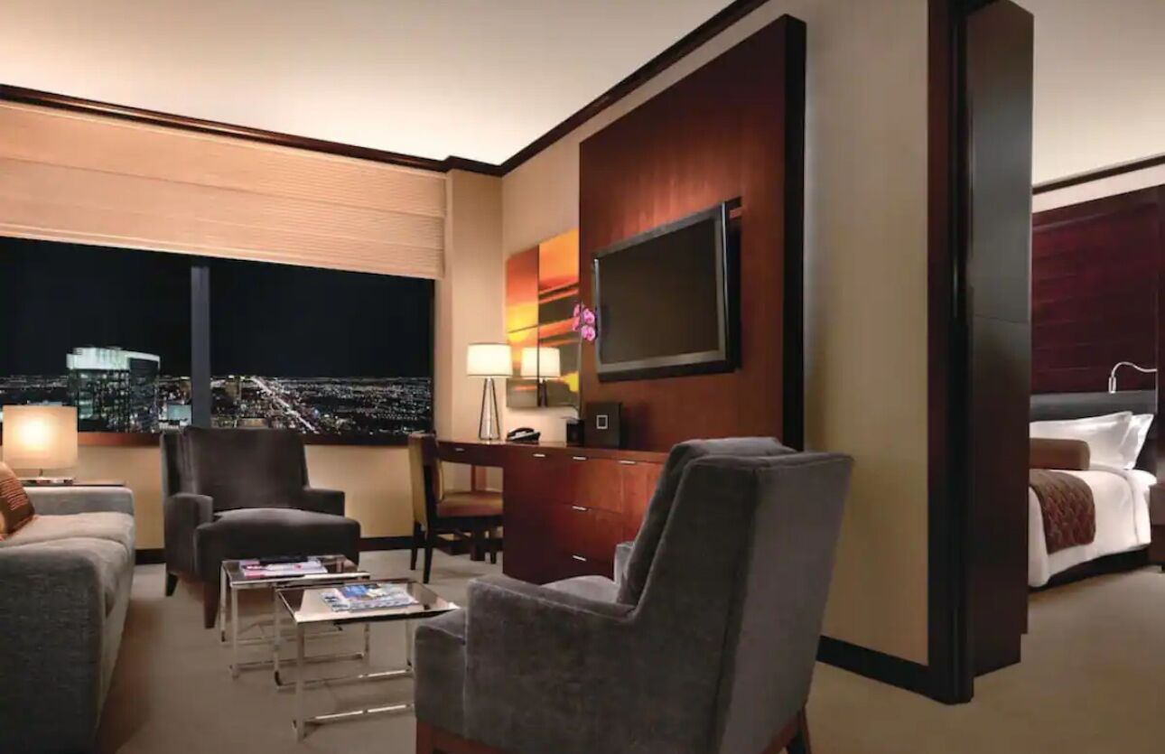 Ein Hotelzimmer mit Blick auf die Stadt, einem flachbildfernseher an der Wand, einem Schreibtisch mit Lampe, einem Sofa und einem Bett.