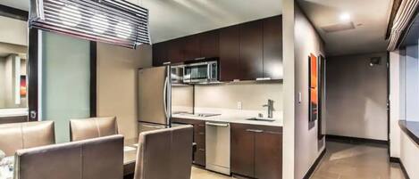 Una cocina moderna con armarios oscuros, un refrigerador de acero inoxidable y un microondas. Cuenta con una zona de comedor con sillas de cuero y una mesa.