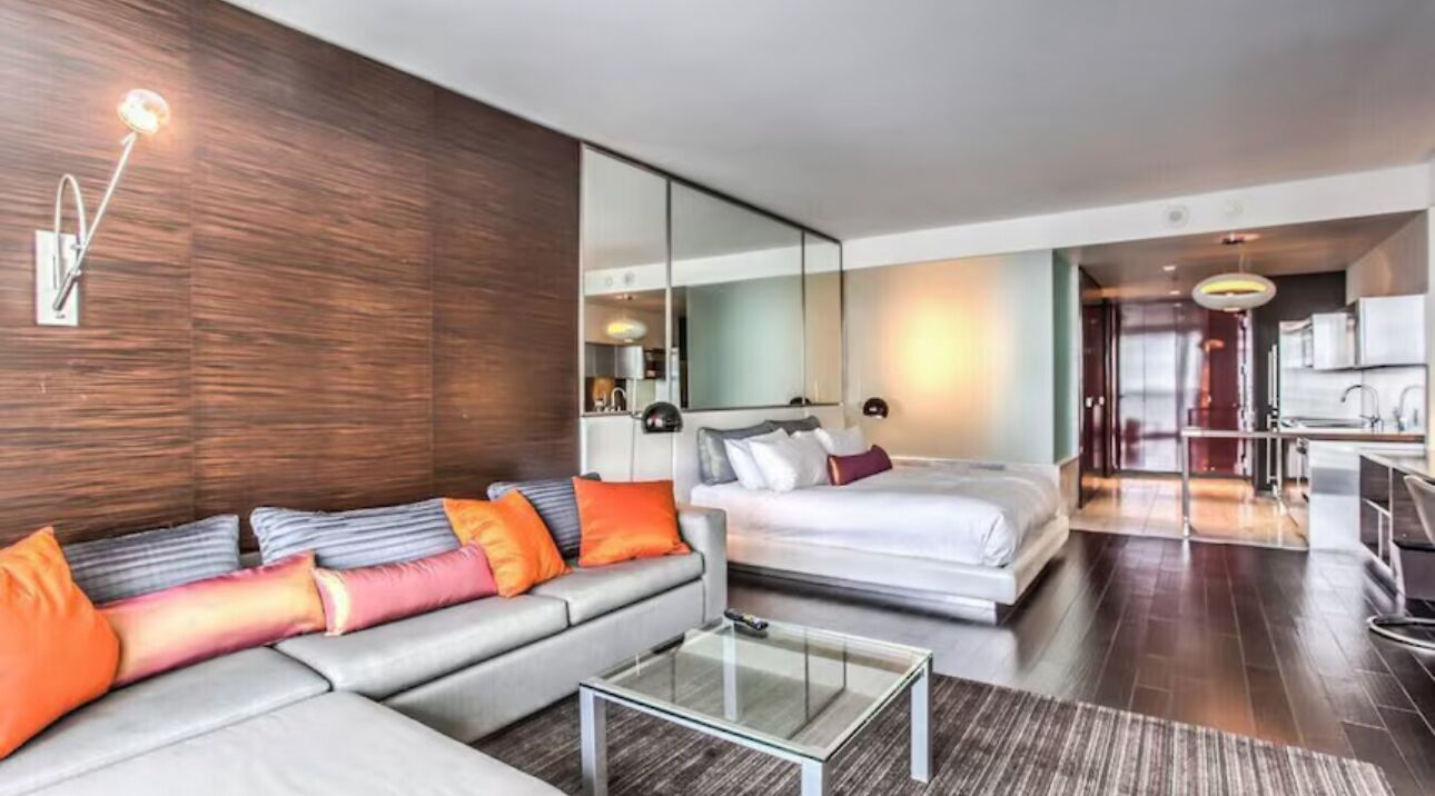 Une chambre d’hôtel moderne avec un grand lit, un canapé, une table basse en verre et un miroir.
