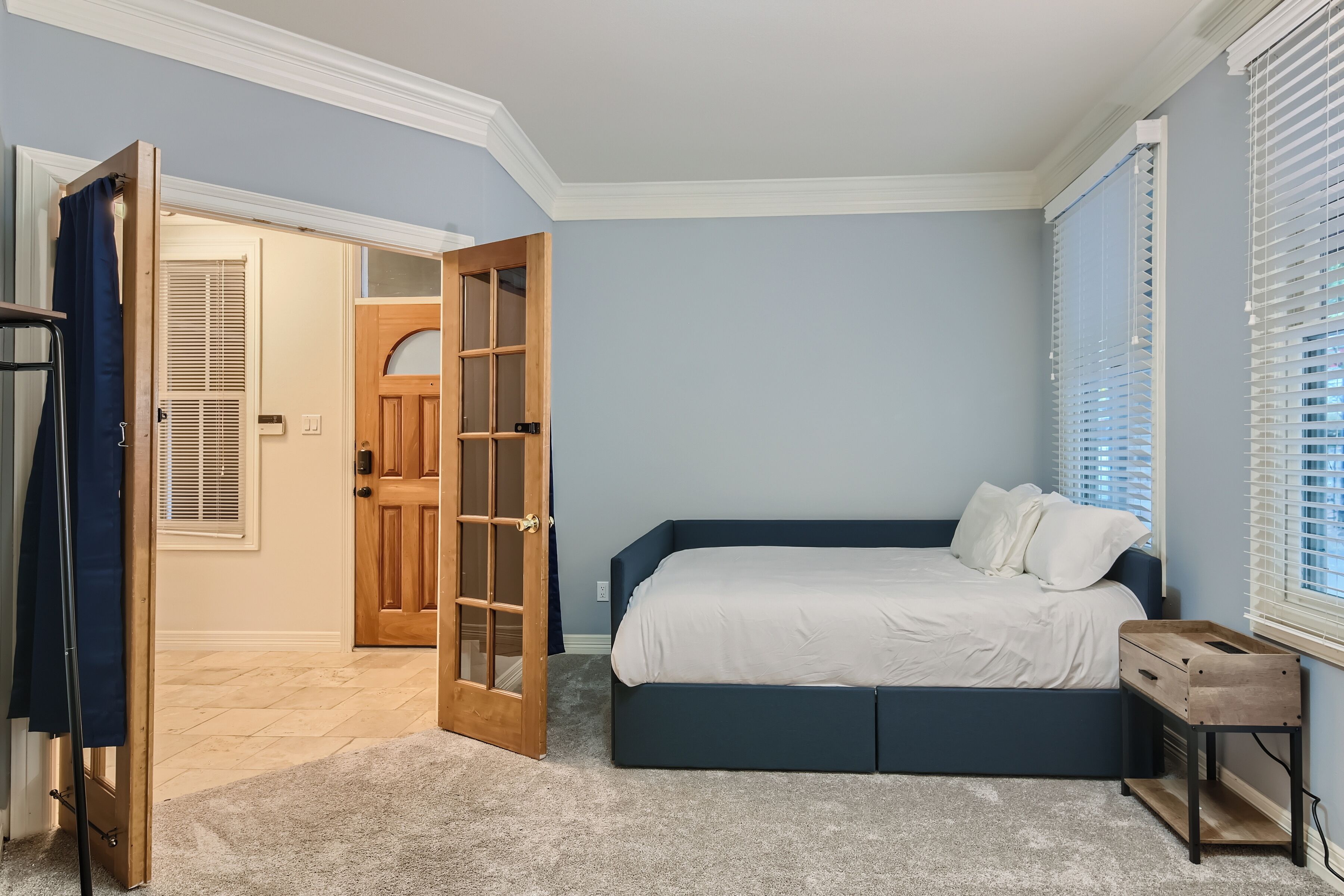 Een slaapkamer met een bed, een houten deur en een raam met jaloezieën.