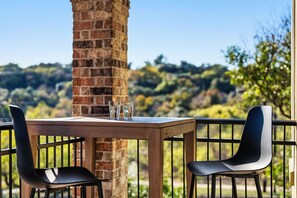 A wooden table with two black chairs and three glasses on it, set against a brick wall with a scenic view of trees and hills in the background. - Townhomes In Downtown Austin  (Austin)