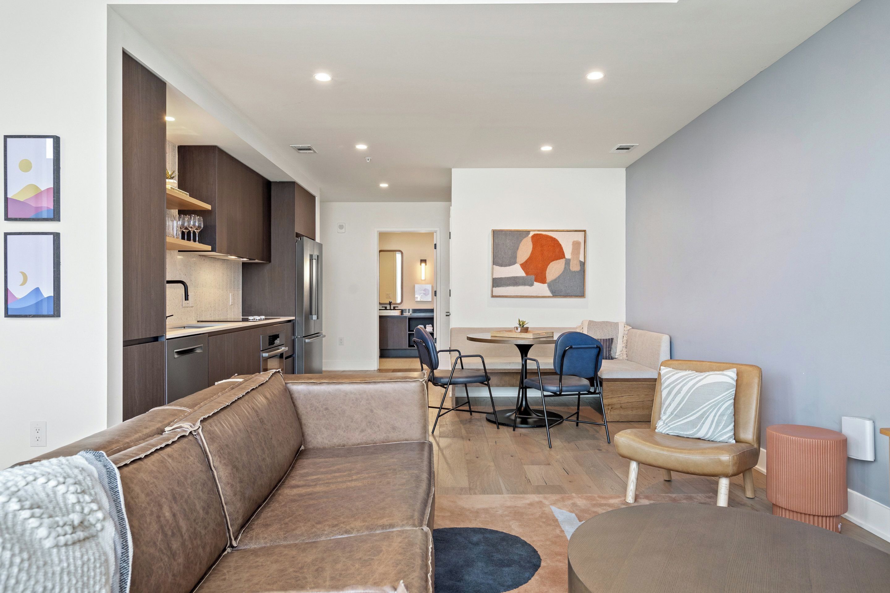 A modern living room with a brown leather sofa, a round coffee table, and a dining area with a small table and chairs.
