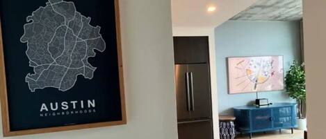 Un soggiorno moderno con una mappa incorniciata dei quartieri di Austin, un frigorifero in acciaio inossidabile, un armadietto blu e un grande quadro astratto appeso al muro.