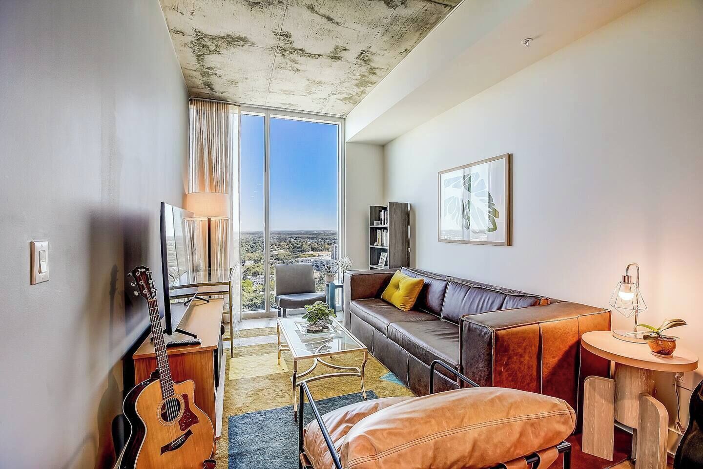 Ein modernes Wohnzimmer mit einer Ledersofa, einem Glastisch und einer Gitarre.