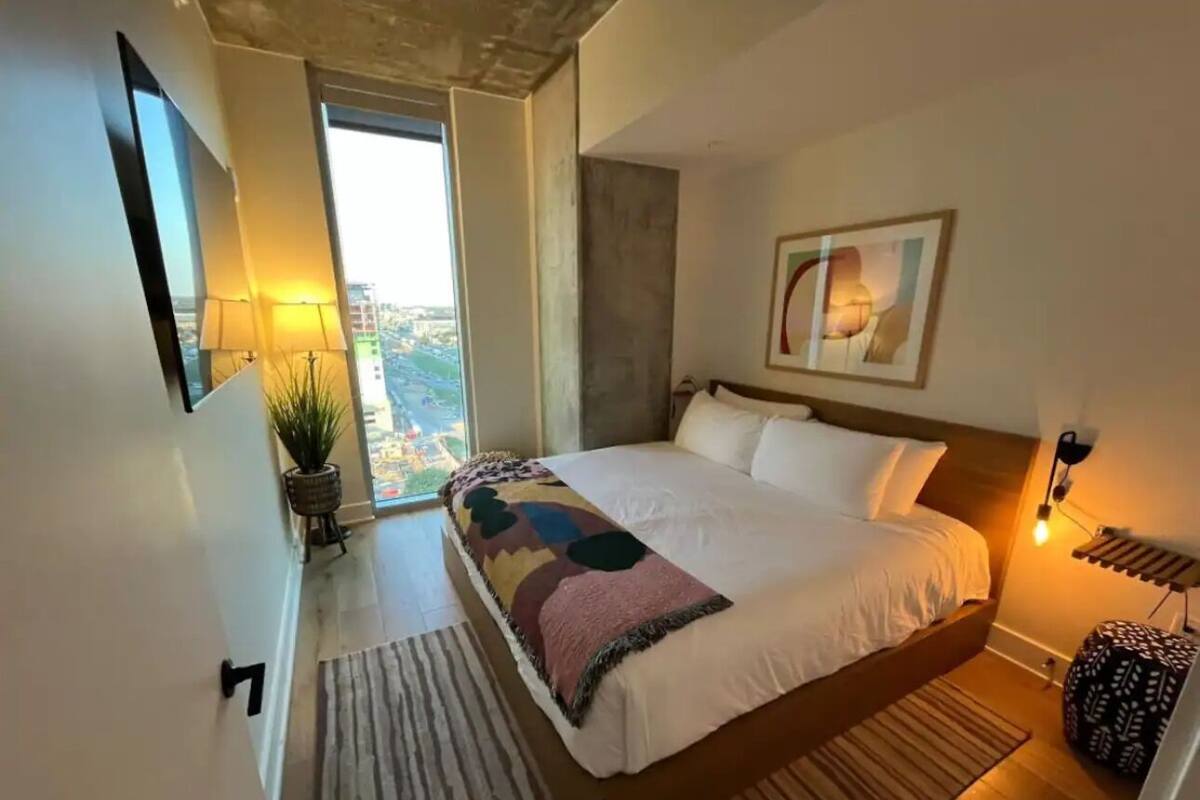 Un dormitorio con una cama grande, vistas a la ciudad, una planta en maceta y una lámpara moderna.