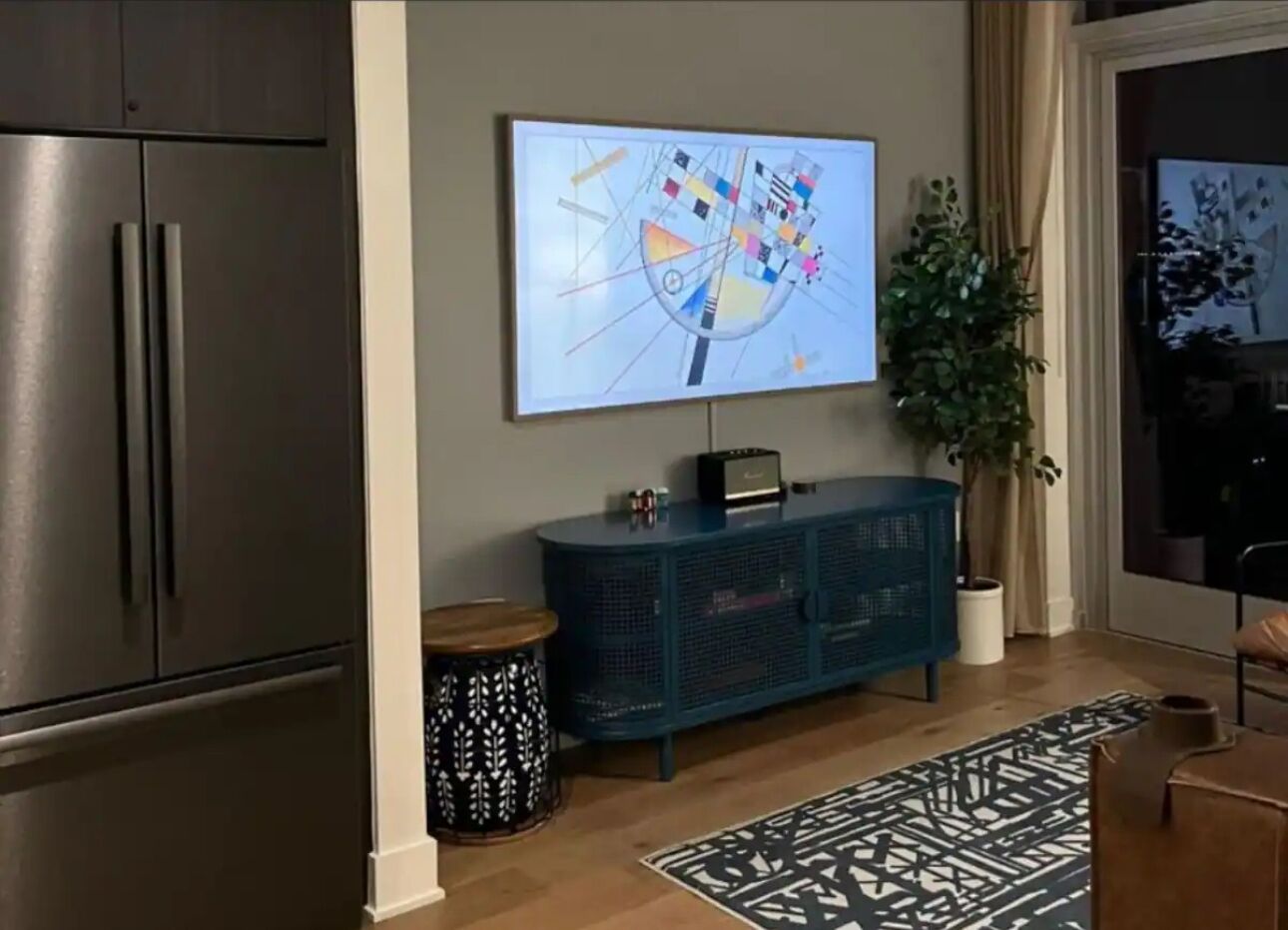Una sala de estar moderna con un televisor de pantalla plana grande montado en la pared, un mueble de color oscuro, un tapete estampado y una planta en maceta.
