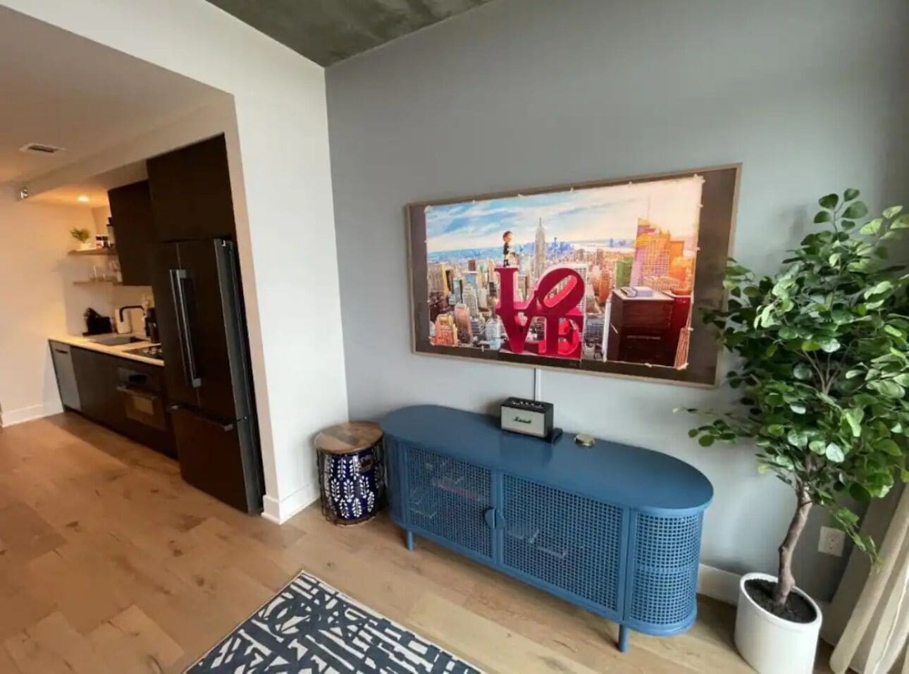 A modern living room with a blue cabinet, a cityscape painting, and a potted plant.