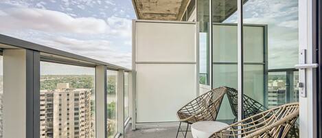 A balcony with large windows, wicker chairs, and a view of a cityscape.