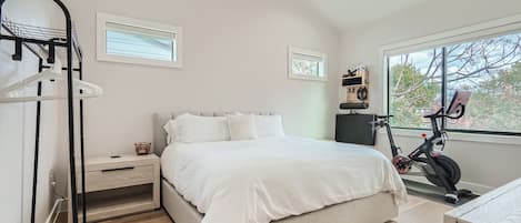 Un dormitorio con cama, mesita de noche, un perchero para bicicletas en la pared y ventana con vista a árboles.