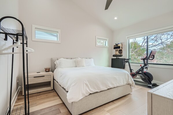 A bedroom with a bed, a nightstand, a wall-mounted bike rack, and a window with a view of trees. - Grand Oasis Ar E.Austin W/Pool (Austin)