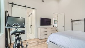 Une chambre avec un lit, un téléviseur fixé au mur, un vélo dans un coin et une armoire à porte coulissante.