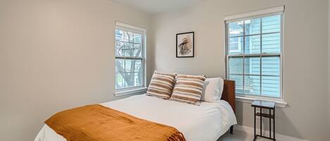 A bedroom with a bed, two windows, a ceiling fan, and a framed picture on the wall.