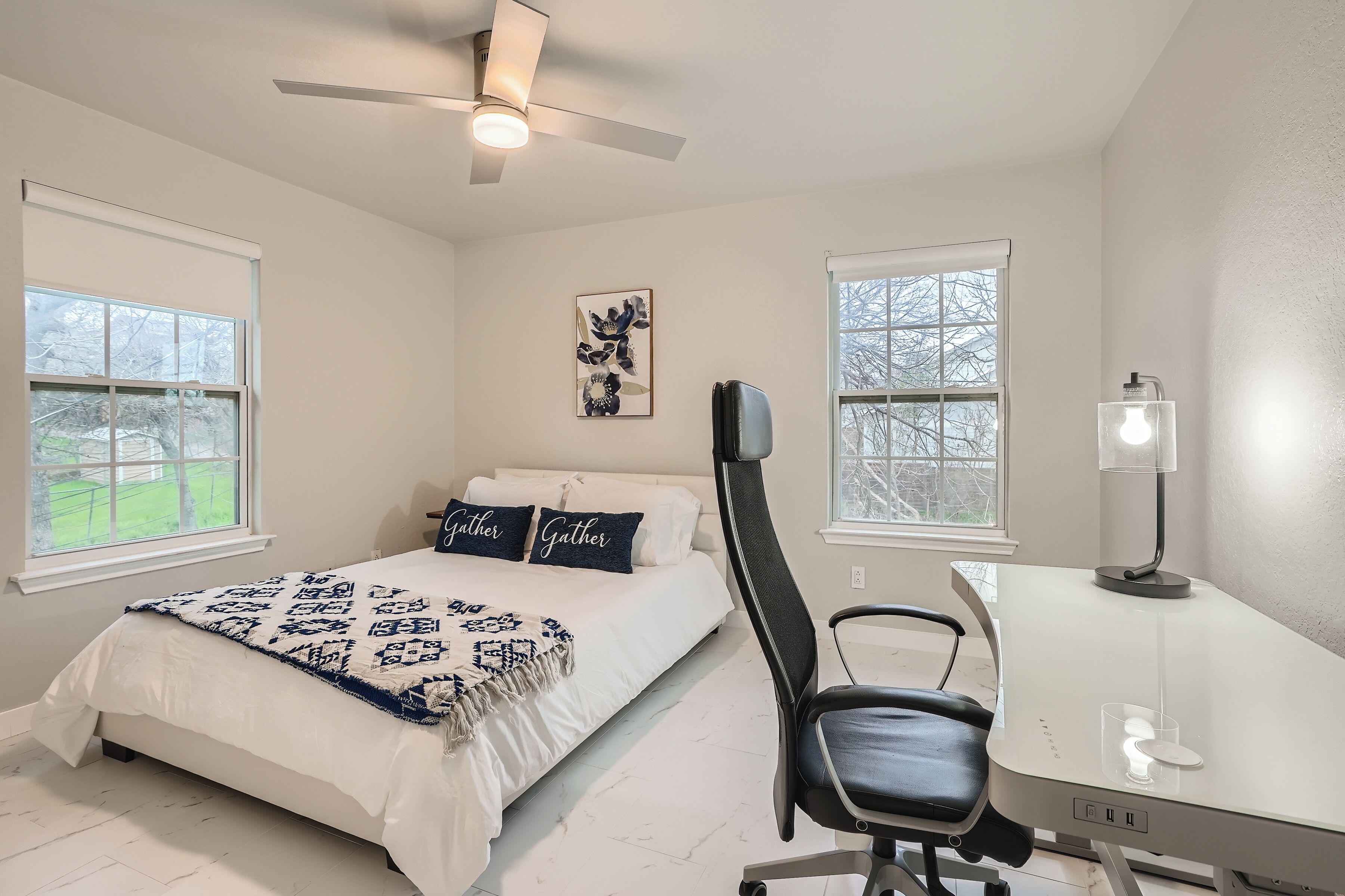 A bedroom with a bed, a desk, a chair, and a ceiling fan.