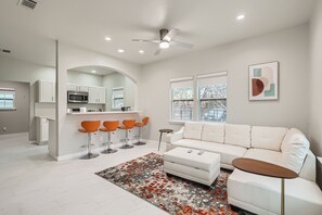 Un salon moderne avec un canapé blanc, des tabourets de bar orange et une table basse.