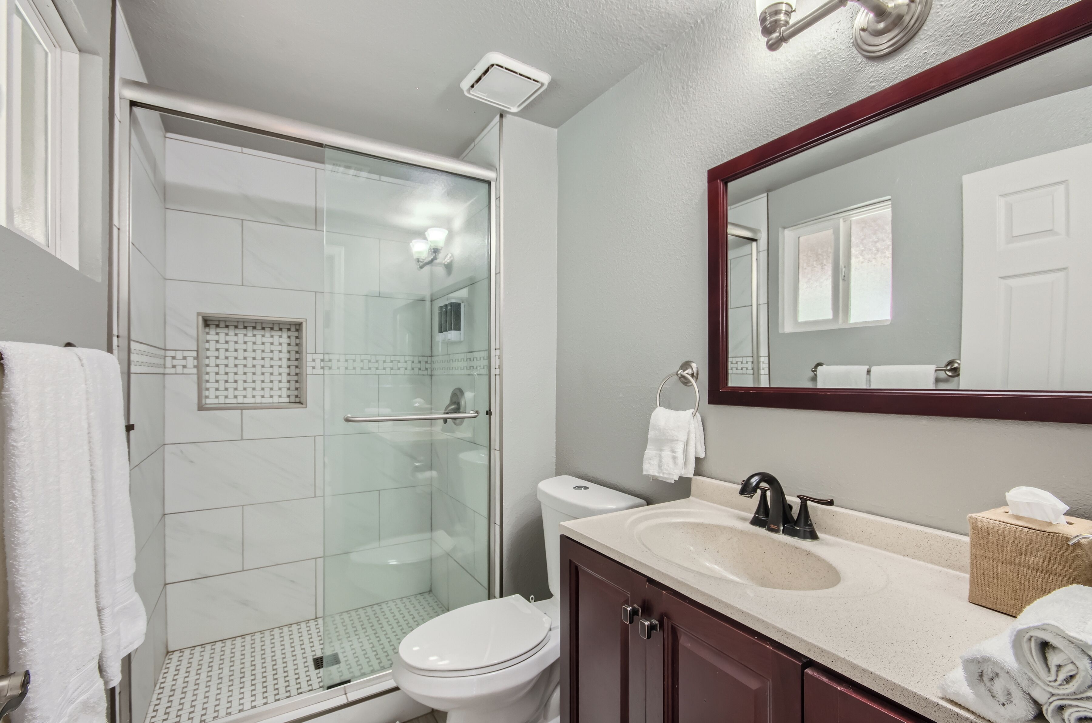 A modern bathroom with a glass-enclosed shower, a white toilet, a sink with a mirror above it, and a towel rack.
