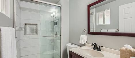 A modern bathroom with a glass-enclosed shower, a white toilet, a sink with a mirror above it, and a towel rack.