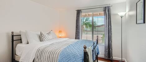 A bedroom with a bed, a bedside lamp, a window with curtains, and a floor lamp.