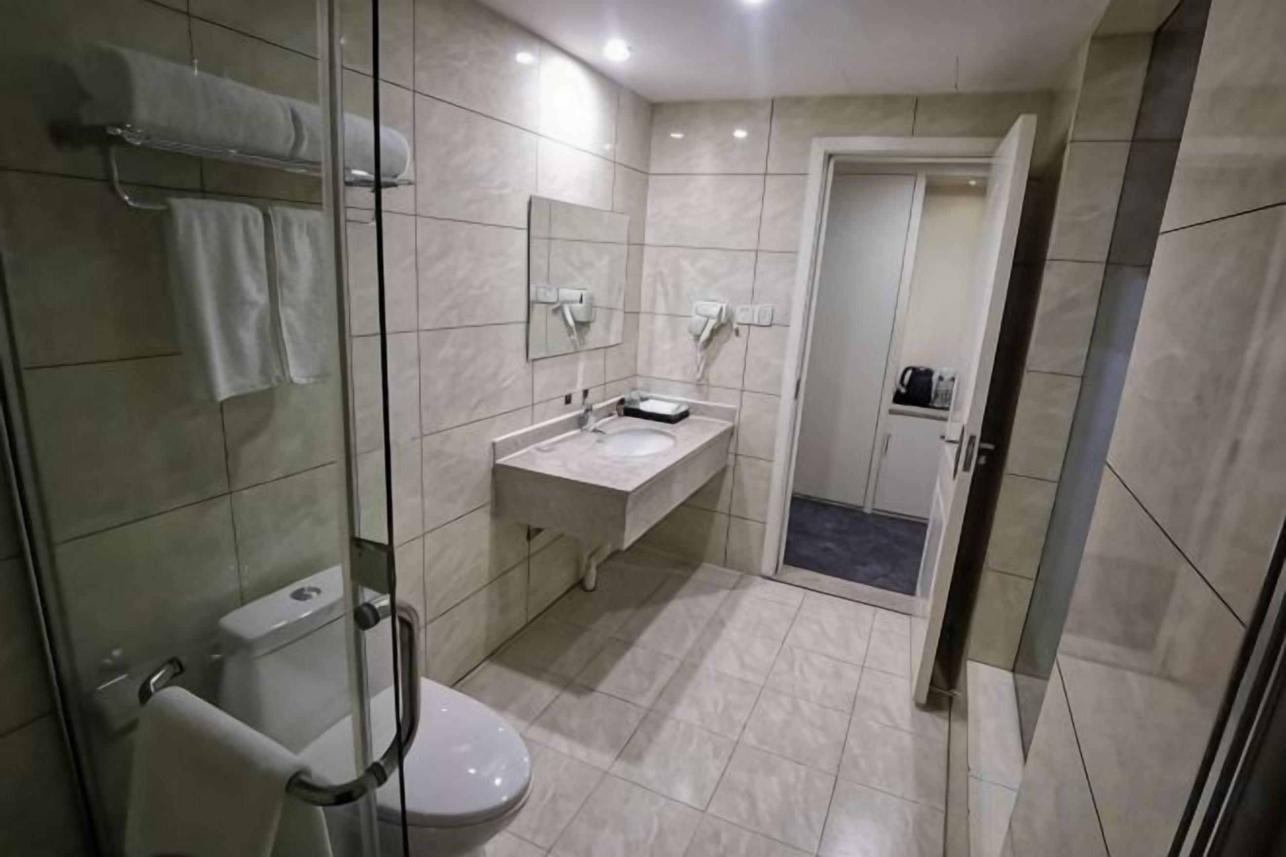 Ein modernes Badezimmer mit einer Duschkabine, einer Toilette, einem Waschbecken mit Spiegel und einer Tür zu einem weiteren Raum.