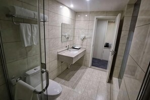 Une salle de bain moderne avec une douche à parois de verre, des toilettes, un lavabo avec un miroir et une porte donnant sur une autre pièce.