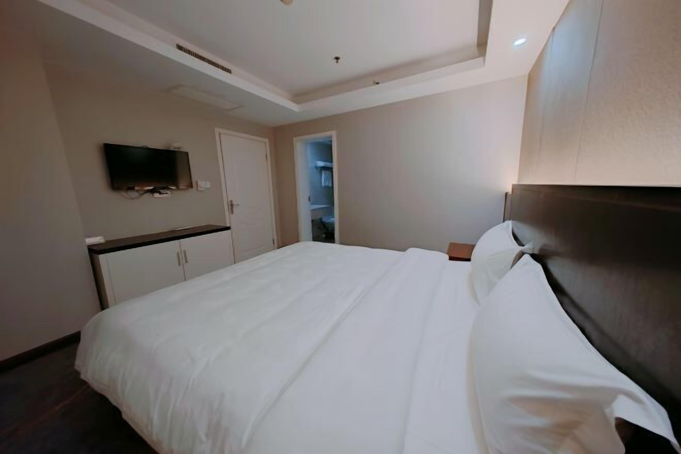 Quarto de hotel com uma cama grande, televisão presa na parede e um guarda-roupa.