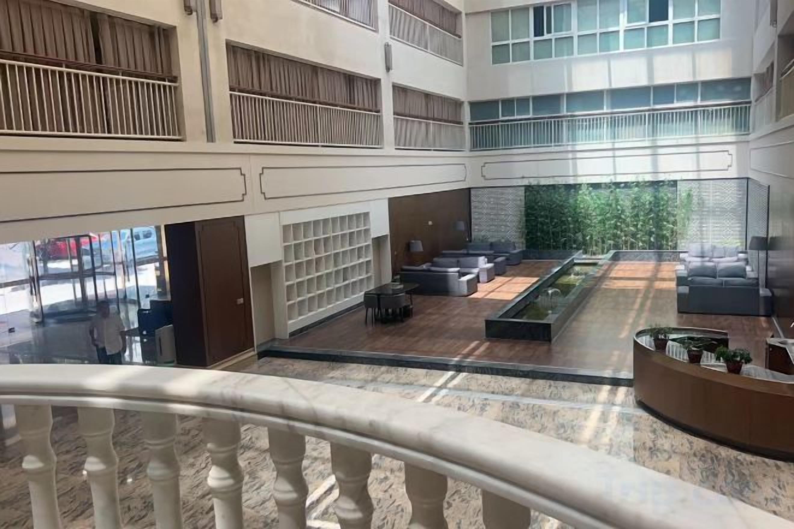 A spacious indoor area with a central seating area, multiple levels with balconies, and a view of greenery outside.