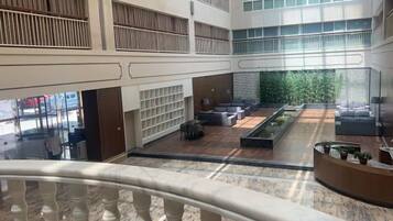 A spacious indoor area with a central seating area, multiple levels with balconies, and a view of greenery outside.