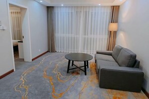 A modern hotel room with a grey sofa, a round table, and a large window with sheer curtains. - Xinshan Hotel (Xinchang)