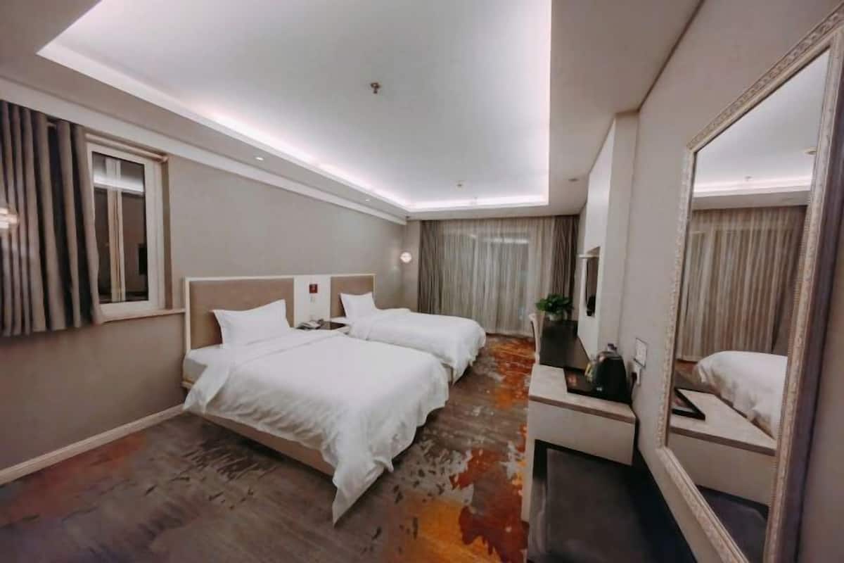 Habitación de hotel con dos camas, un escritorio, un espejo y una lámpara en el techo.