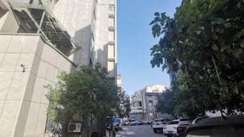 A narrow urban street with parked cars, trees, and buildings.