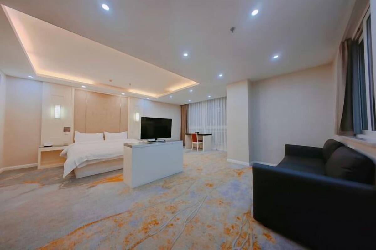 Una habitación de hotel moderna con cama, televisión, sofá y zona de comedor.