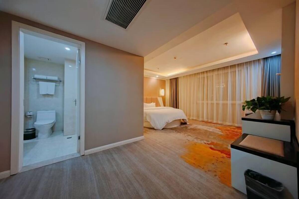 Una habitación de hotel con cama, baño, escritorio y una planta.