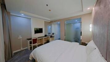 Habitación de hotel con una cama grande, un escritorio, una silla, un televisor y un espejo.