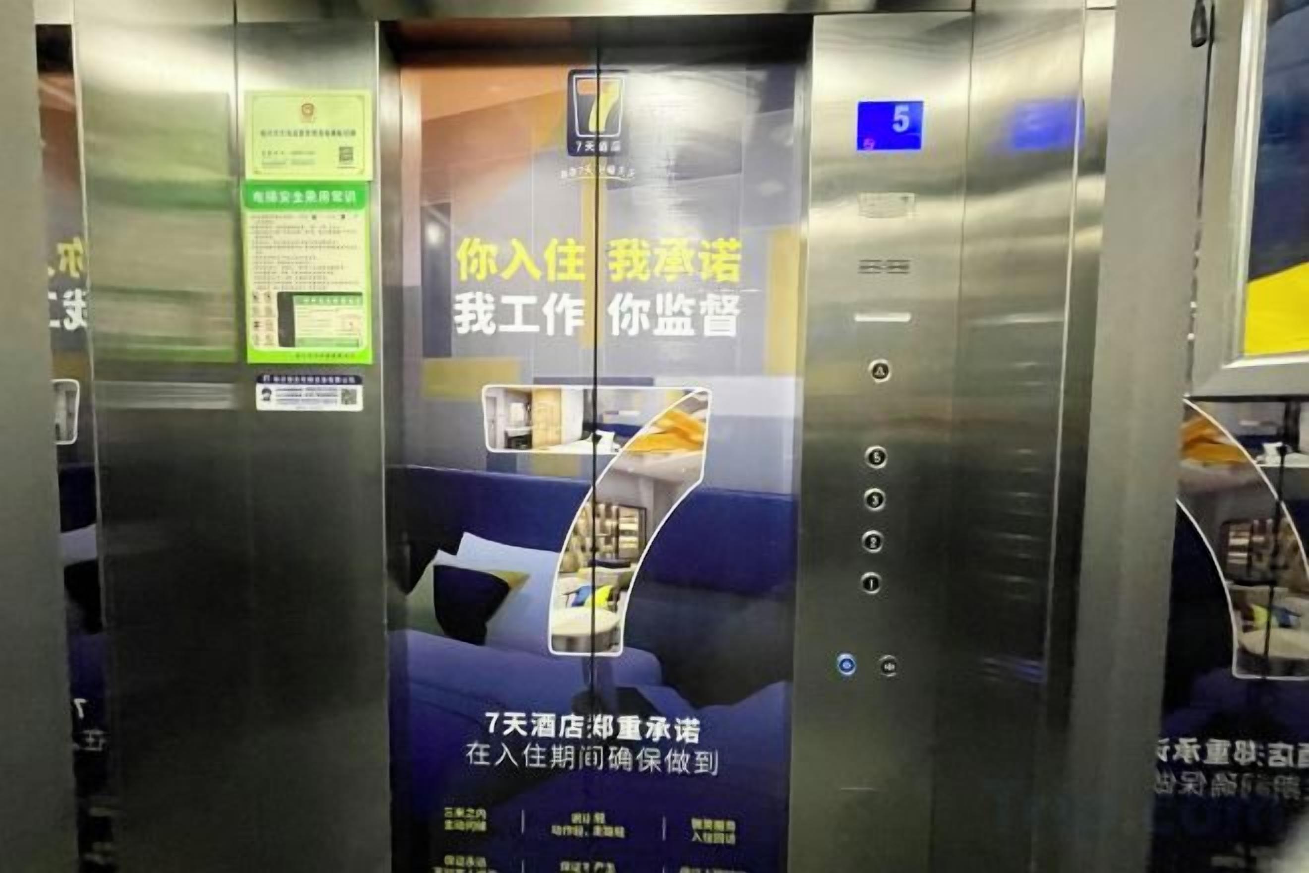 Interior de elevador com visor digital mostrando o andar 5, um cartão com informações de segurança e um anúncio promocional.