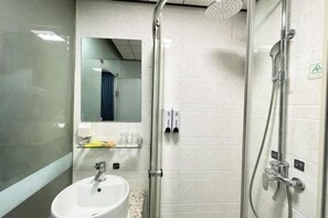 Un baño moderno con ducha de vidrio, lavabo blanco y espejo sobre él.