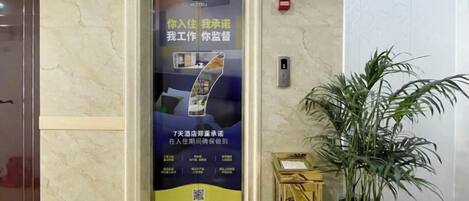 Un ascensor con un cartel publicitario, una planta en maceta y un piso de mármol.
