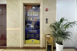 Un ascensor con un cartel publicitario, una planta en maceta y un piso de mármol.