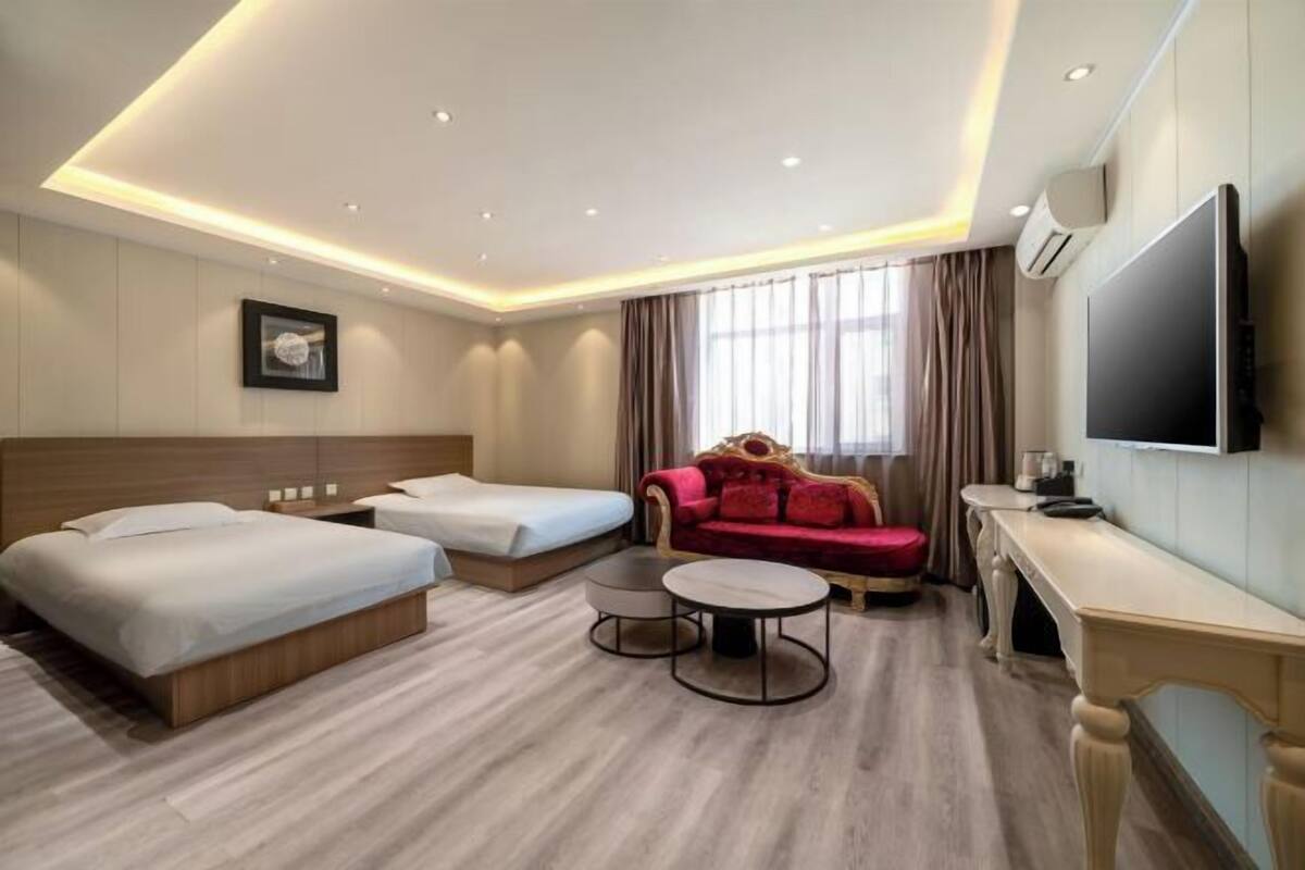 Ein Hotelzimmer mit zwei Betten, einem Sofa, einem Fernseher und einem Schreibtisch.