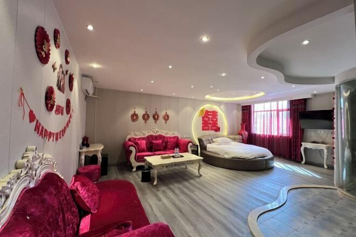 A modern hotel room with a red sofa, a round bed, and a dining table.