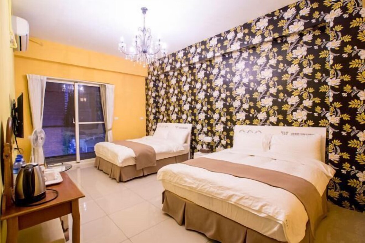 Une chambre d’hôtel avec deux lits, un lustre, une table avec une bouilloire et une fenêtre avec des rideaux.