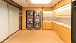 A compact laundry room with two front-loading washing machines, wooden cabinetry, and a tiled backsplash. - JI Hotel (Huzhou Dongwu Intime City Renhuangshan Store) (Huzhou)