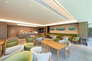 A modern interior with tables and chairs arranged in a casual dining area, a counter with a display, and a wall with abstract art. - JI Hotel (Huzhou Dongwu Intime City Renhuangshan Store) (Huzhou)