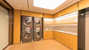 A modern laundry room with two front-loading washing machines, wooden cabinetry, and a tiled backsplash. - JI Hotel (Huzhou Dongwu Intime City Renhuangshan Store) (Huzhou)