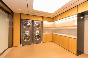 A modern laundry room with two front-loading washing machines, wooden cabinetry, and a tiled backsplash. - JI Hotel (Huzhou Dongwu Intime City Renhuangshan Store) (Huzhou)
