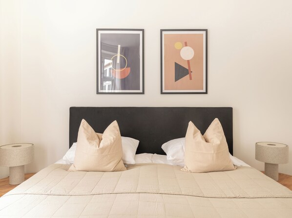 Un lit bien fait, avec deux oreillers, une tête de lit sombre et deux œuvres d’art abstraites encadrées accrochées au mur.