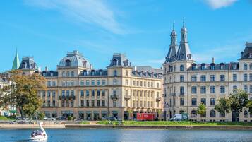 A historic building with classical architecture, a river in the foreground, and a swan-shaped boat with people.