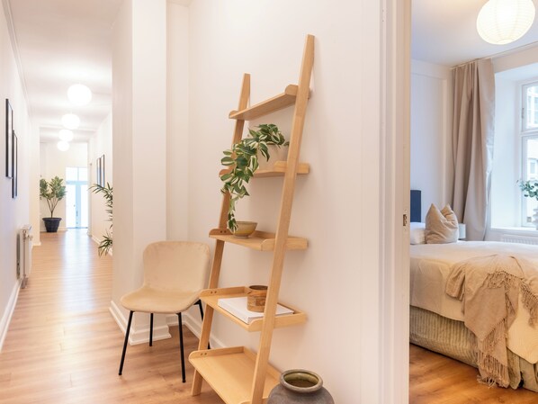 A modern interior with a wooden ladder shelf holding plants and a bowl, a chair, and a bed with a window view. - Noble - Fantastic 5-bdr Apt in the Capital (Copenhagen)